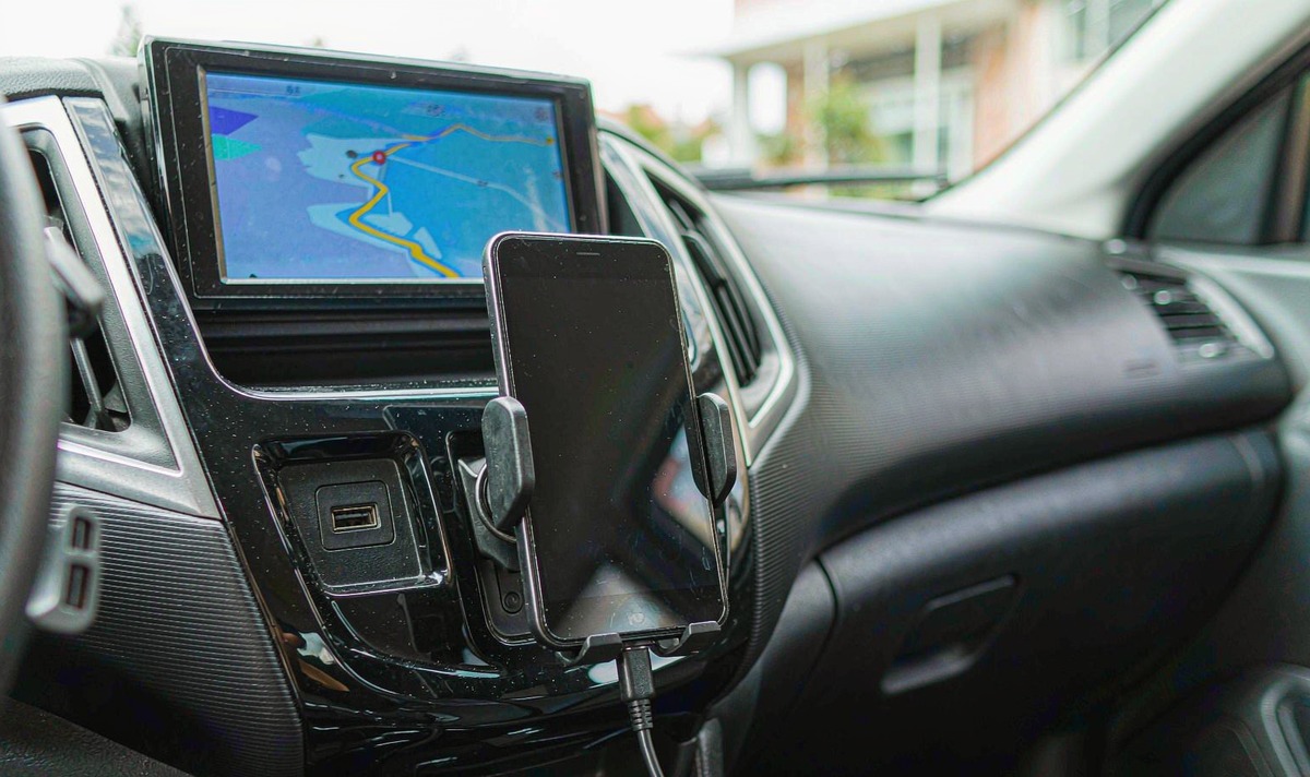 Phone held in a centre console cradle with a USB charging lead running down into the dashboard socket while an aftermarket touchscreen head unit above it shows a navigation map