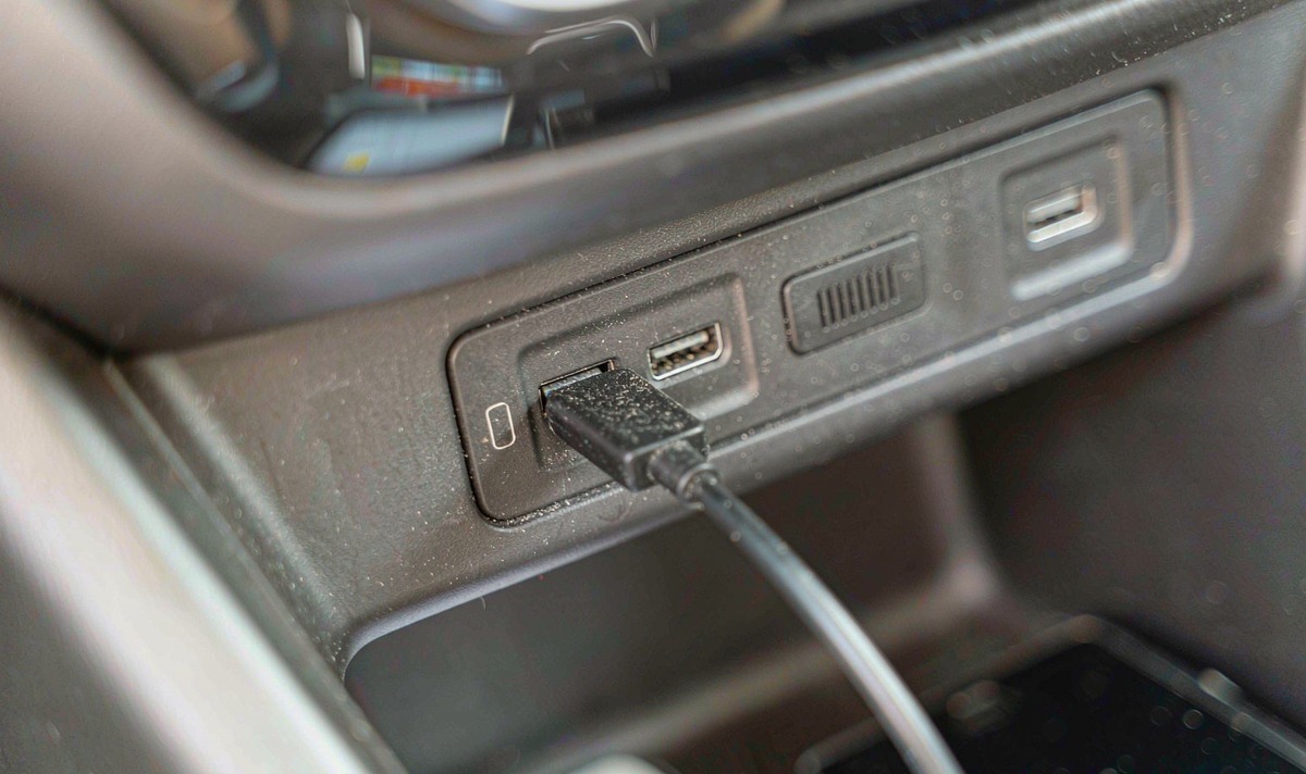 Close-up of two USB sockets set side by side in a car centre console with a charging lead plugged into the socket that carries the smartphone pictogram