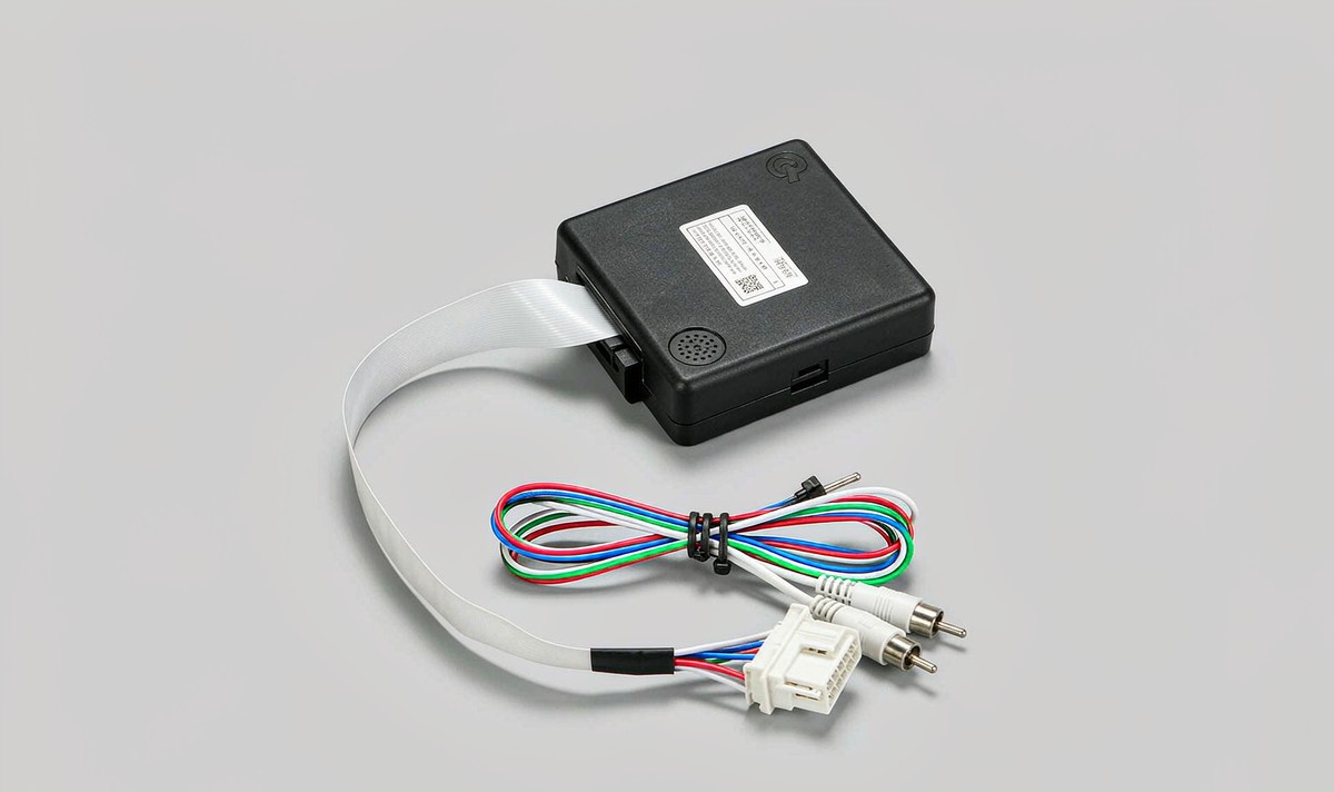 Matte black CANBUS decoder box with a white model label and a beeper grille, its ribbon cable running into a harness bundle with a white multi-pin socket and RCA plugs