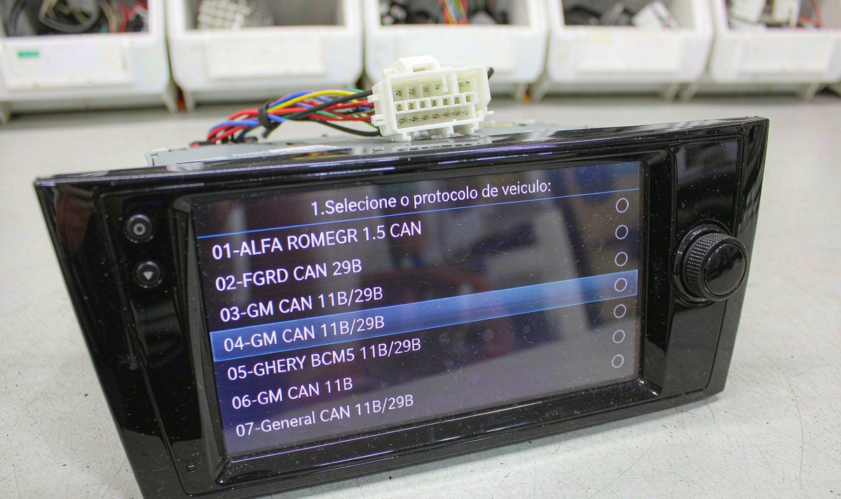 Aftermarket Android head unit on a bench showing a factory settings list of vehicle protocols, with one entry highlighted