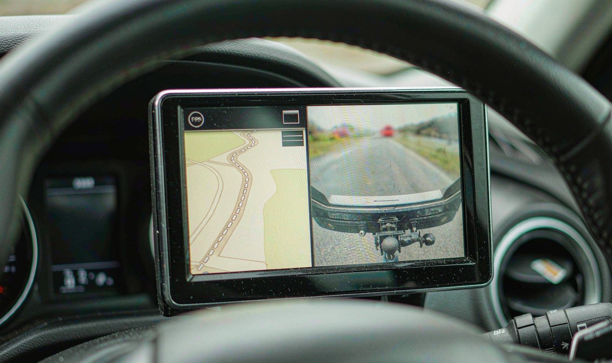 Small 7-inch car radio screen split into two halves, a simple map on the left and a rear camera view of a trailer hitch on the right