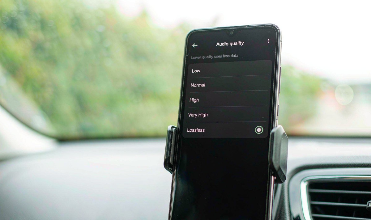 Phone in a car mount showing a music app audio quality page with Low, Normal, High, Very High and Lossless rows, the Lossless row selected