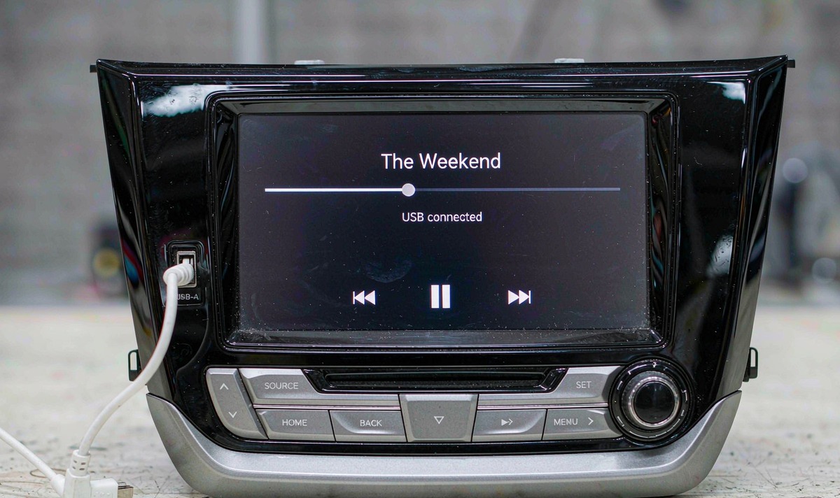 Car head unit on a workbench with a cable plugged into its front USB port and a USB connected message with a playback bar on the screen