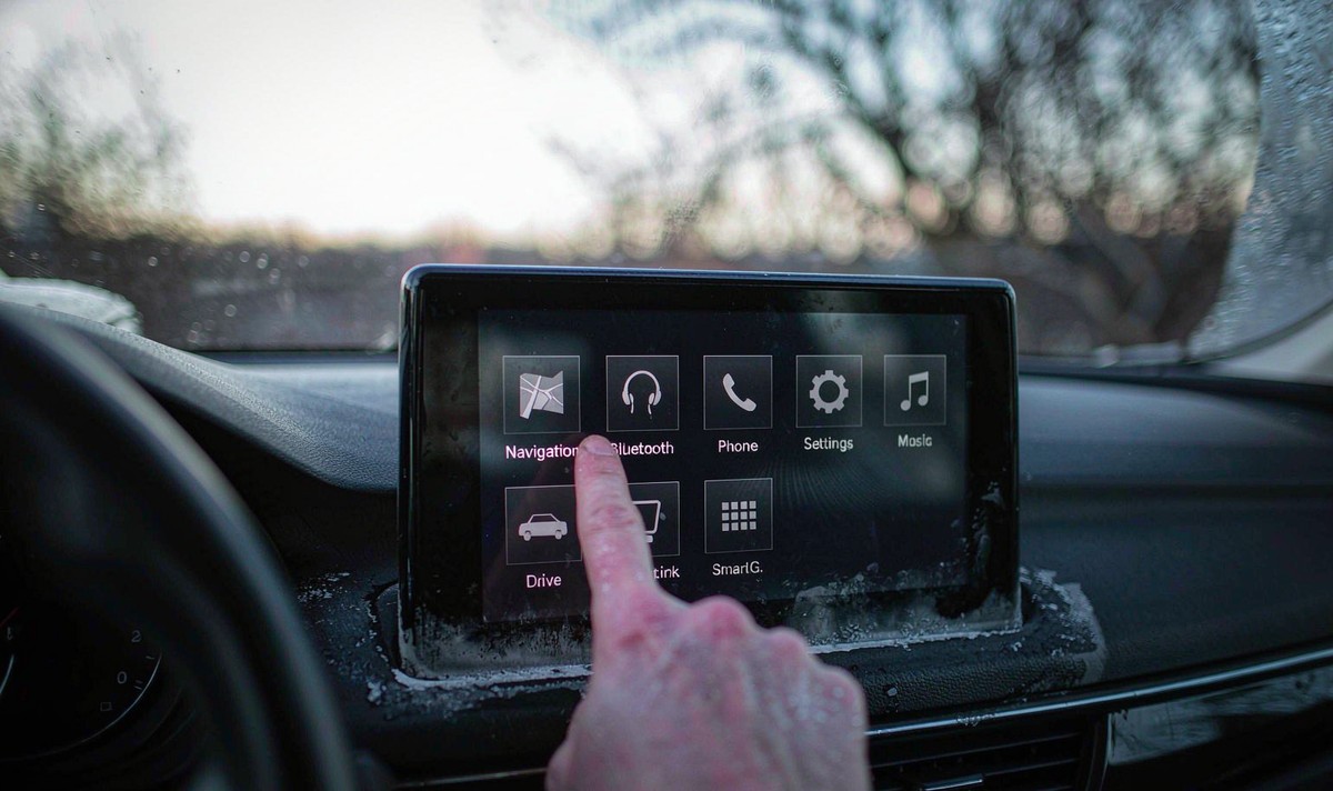 Driver's finger tapping the Navigation button on a cold car radio touchscreen while a pale haze of condensation sits along the bottom edge of the glass