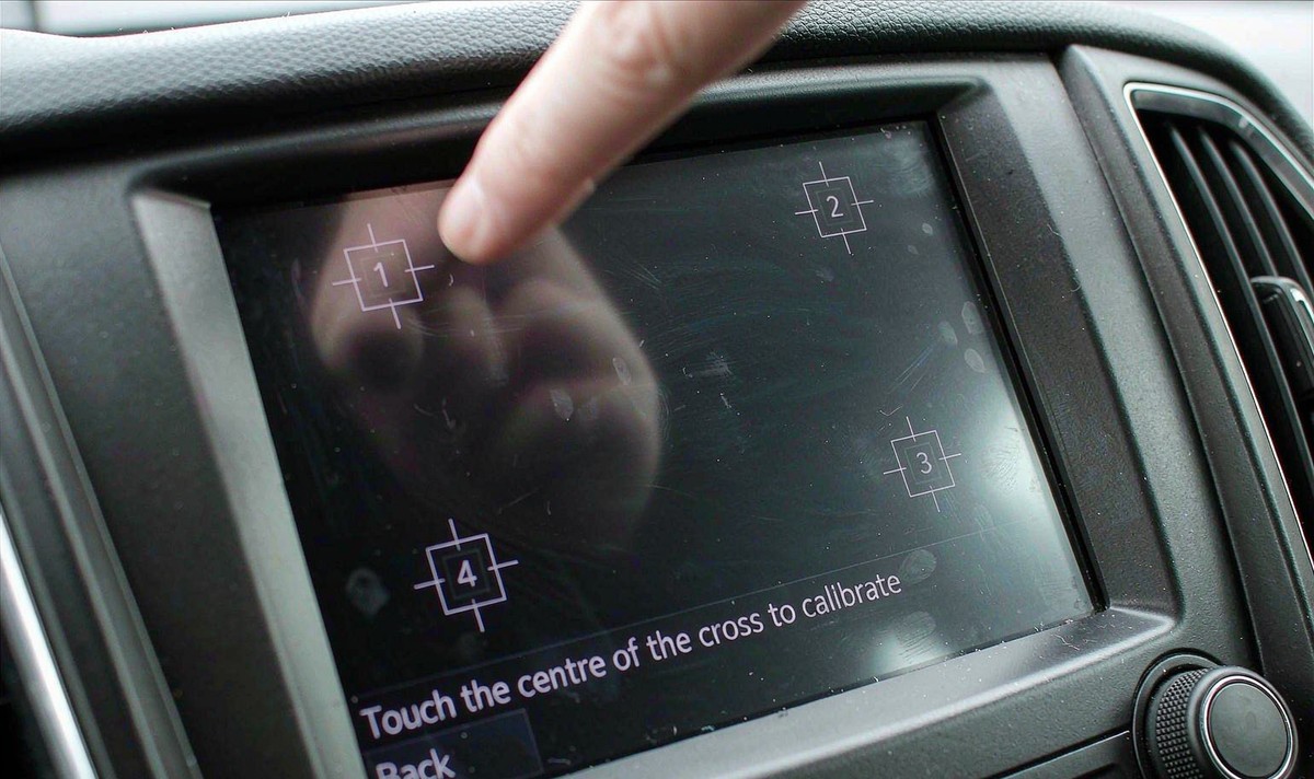 Car radio touch calibration screen showing a numbered target in each corner and a small crosshair prompt on the glass of a retrofit Android head unit