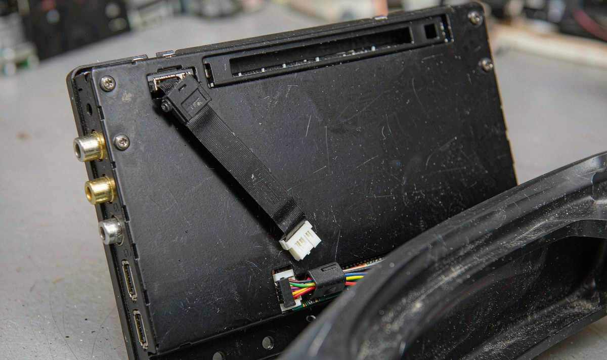 Rear of a retrofit Android car radio with the wide touch panel flex cable and its hinged latch connector visible above the main board