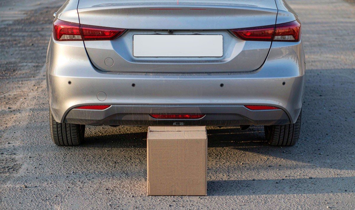 Cardboard box placed on flat pavement behind a parked car to check where the reversing camera far guide line lands
