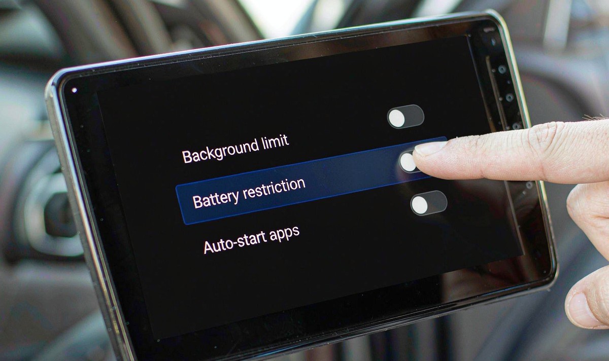Finger tapping a toggle on a car head unit settings page listing background limit, battery restriction and auto-start apps rows