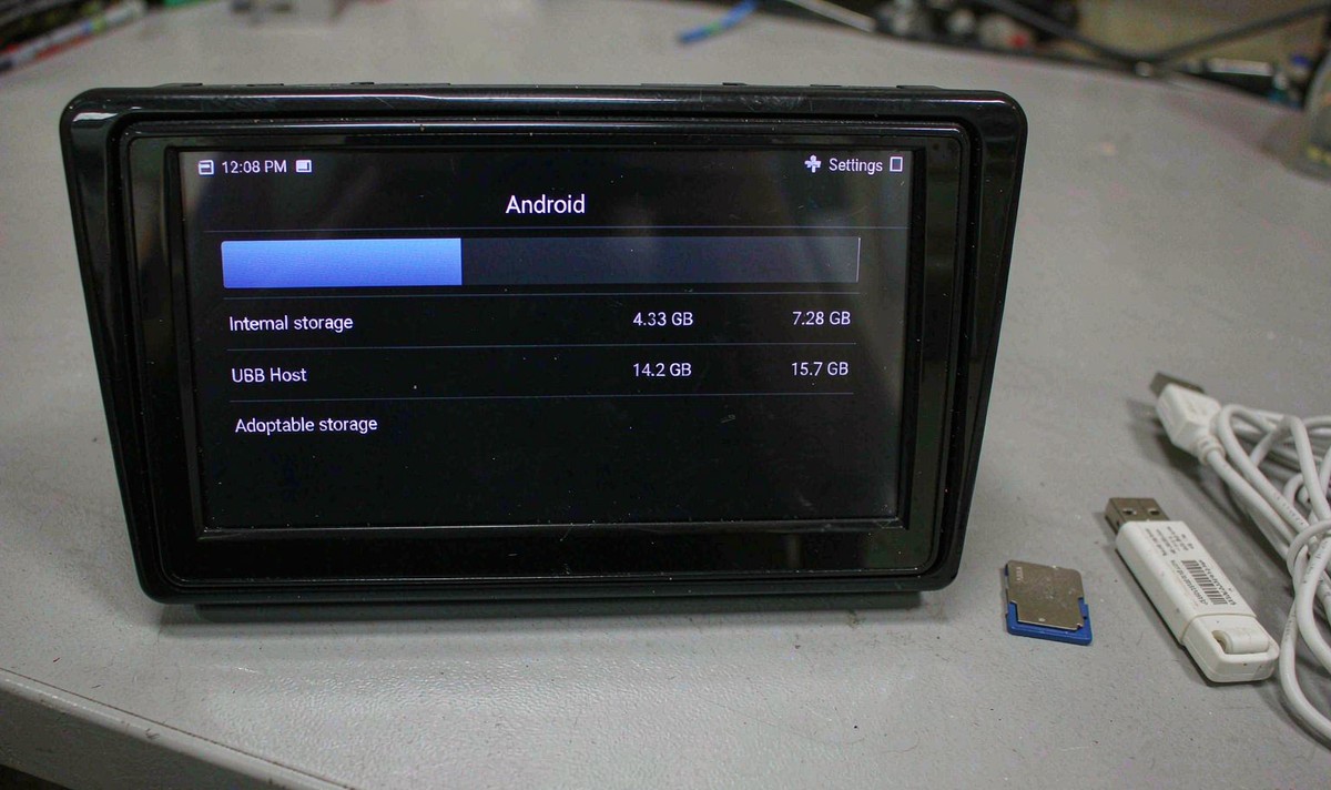 Car head unit storage screen listing internal storage and USB host usage beside a microSD card and USB drive on a bench