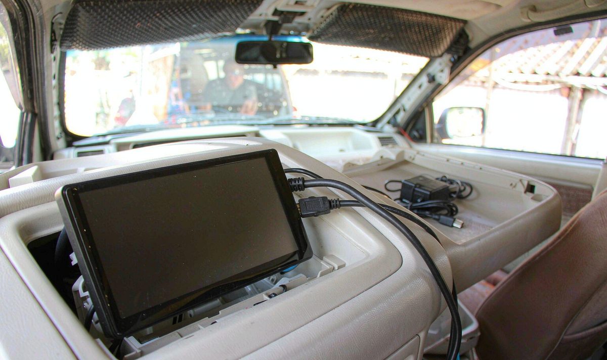 A car dashboard screen reporting no signal with an HDMI cable plugged into the harness behind it, next to a small powered adapter box and a spare short cable