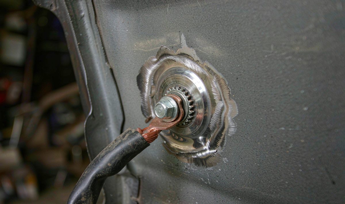 A ring terminal and star washer bolted to a patch of bare metal where paint has been sanded off a car chassis