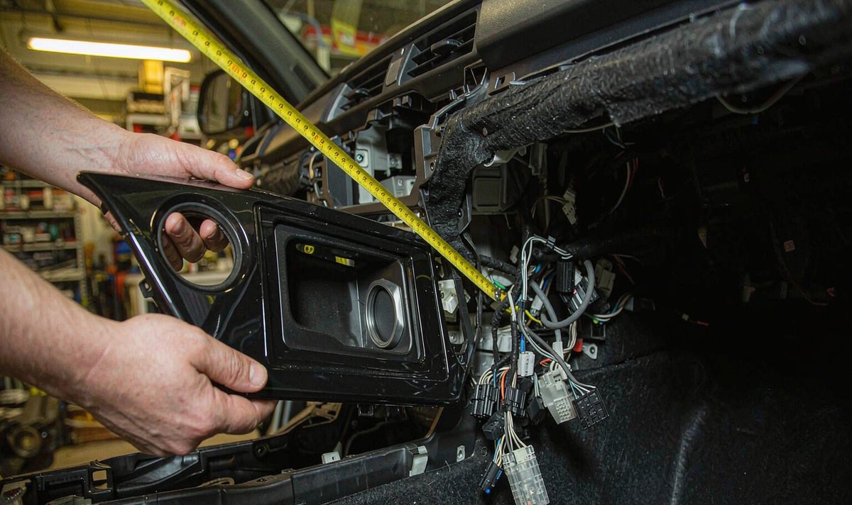 Measuring a dashboard opening with a tape measure while holding an android head unit aftermarket dash kit frame against the slot