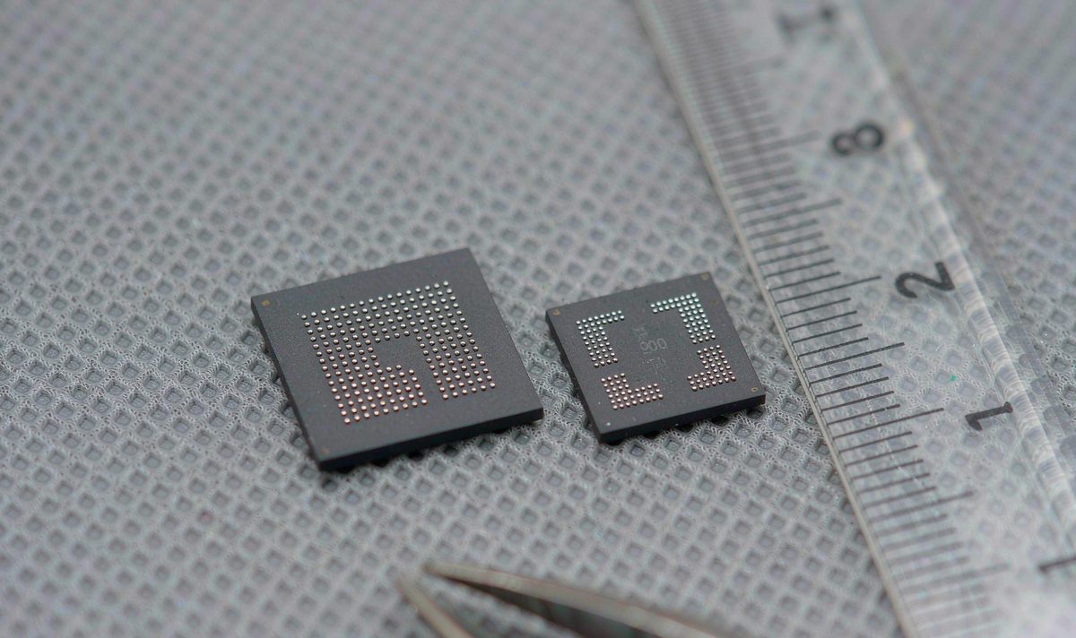 Two matte black flash memory chip packages side by side on an anti-static mat next to a ruler, car head unit storage parts, one package slightly larger than the other