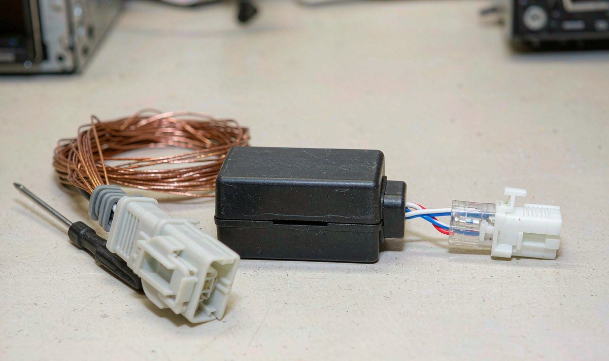 Small CAN bus decoder box and car stereo wiring harness adapter on a workbench, with the twisted CAN pair and its white connector laid out beside it