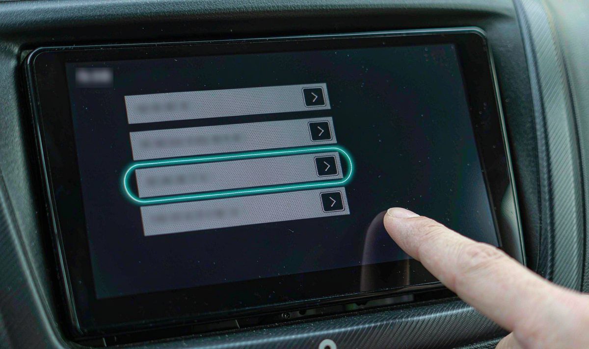 Settings menu on an android car radio screen with four vehicle profile option rows and a finger tapping one, retrofit head unit mounted in a dashboard