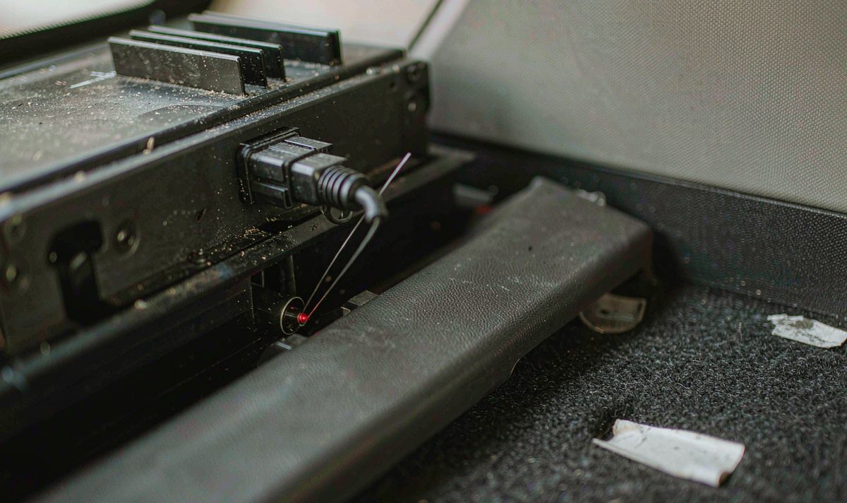 Optical fibre connector unplugged from the socket on the back of a factory car amplifier, a car stereo retrofit job, the bare fibre tip carrying a faint red glow