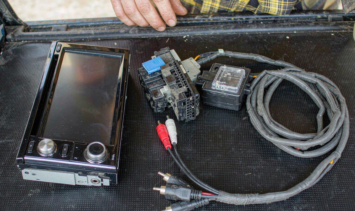 Retrofit android car head unit on a bench beside a vehicle specific wiring harness adapter with its connector block and a pair of RCA pre-out cables, car stereo amplifier wiring