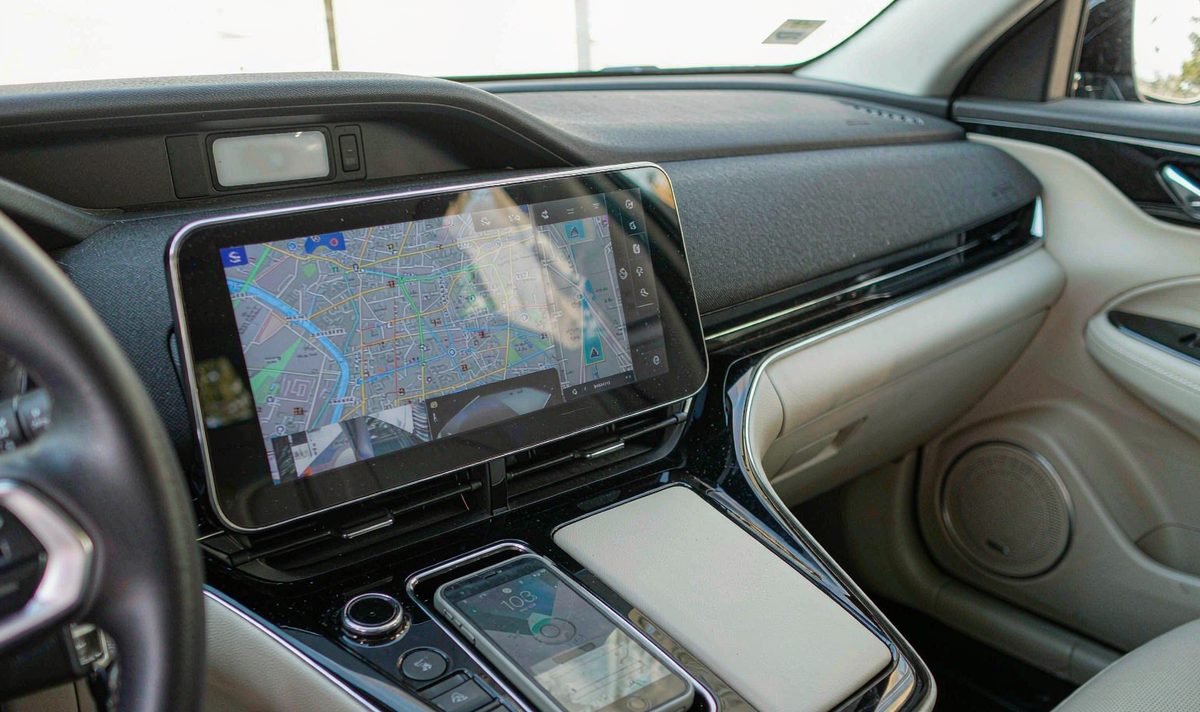 Phone lying unplugged in the centre console of a car while a retrofit car screen in the dashboard mirrors its navigation, an android head unit connection with no cable between them