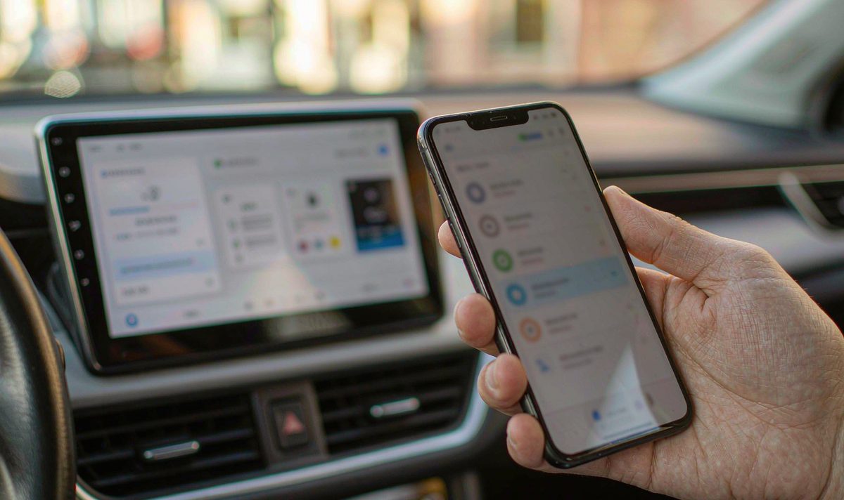 Hand holding a phone beside a lit car screen, the phone showing its saved Bluetooth device list with the car kit entry highlighted, an android head unit bluetooth pair that keeps dropping