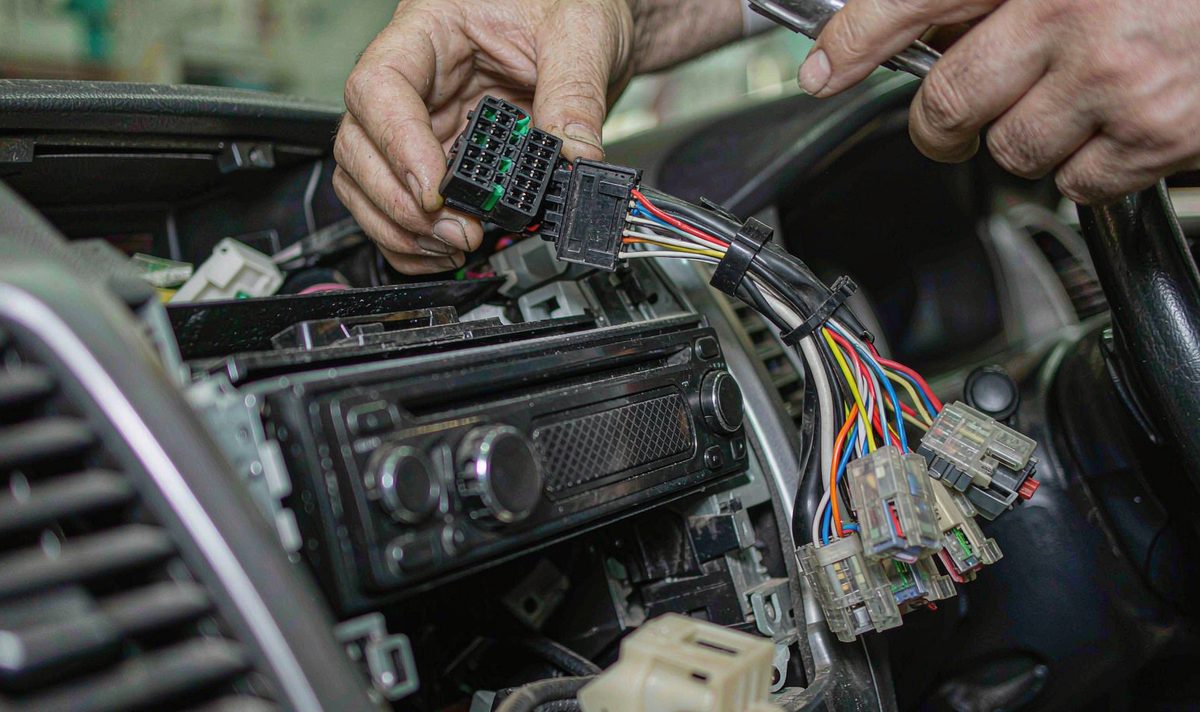 Factory JBL audio harness android head unit aftermarket dash kit, retain original factory features, a multi-pin radio connector being unplugged behind a car centre console