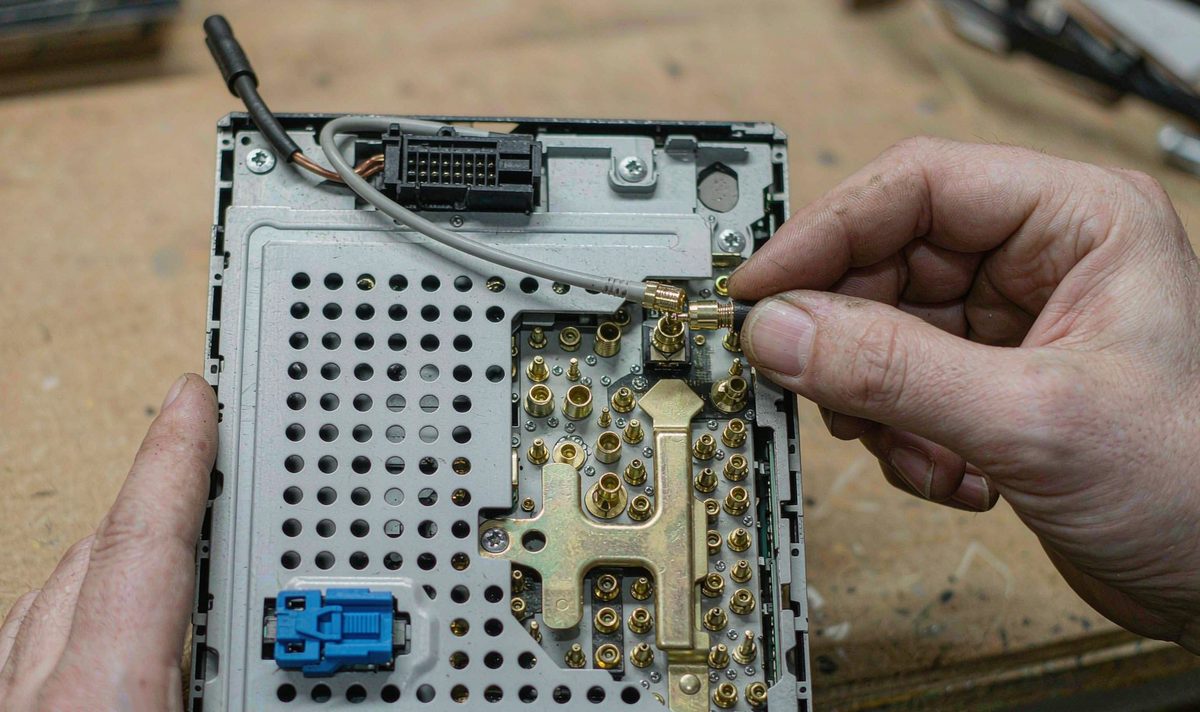 The GPS port on the back of an aftermarket head unit takes a thin coax lead with a small threaded plug Technician fitting the threaded SMA connector of a GPS antenna lead to the back panel of an aftermarket car head unit
