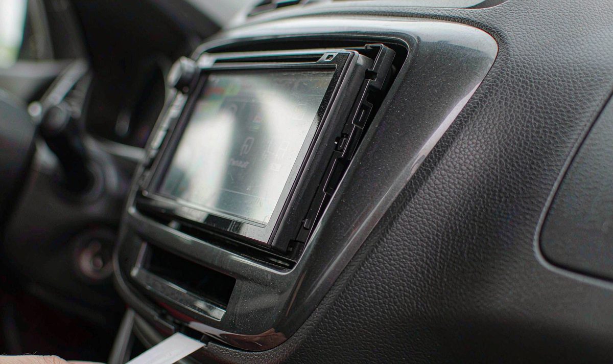 Car screen fascia panel fitted in a dashboard with a visible gap along the top edge, a card held into the seam to gauge it