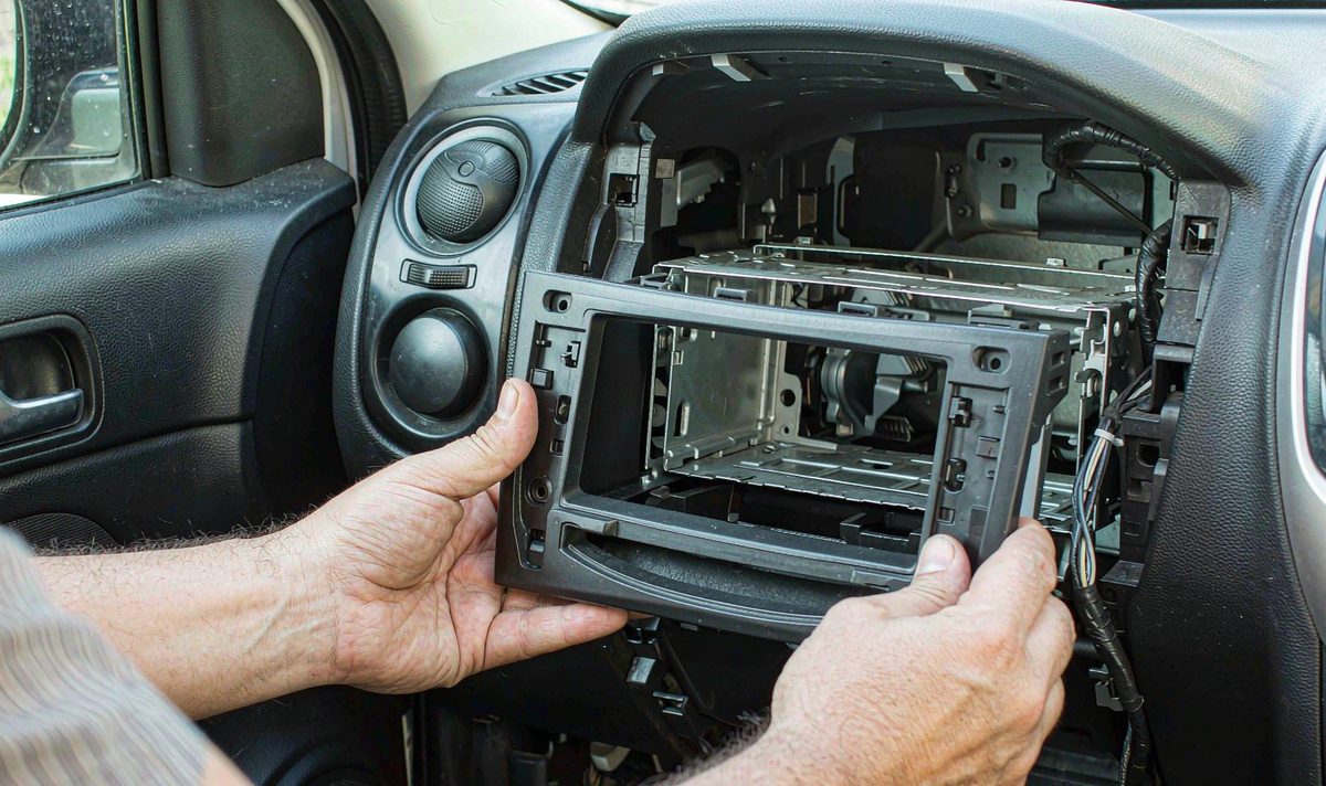 Technician dry fitting a bare black plastic car dash fascia panel into an empty factory radio aperture before wiring